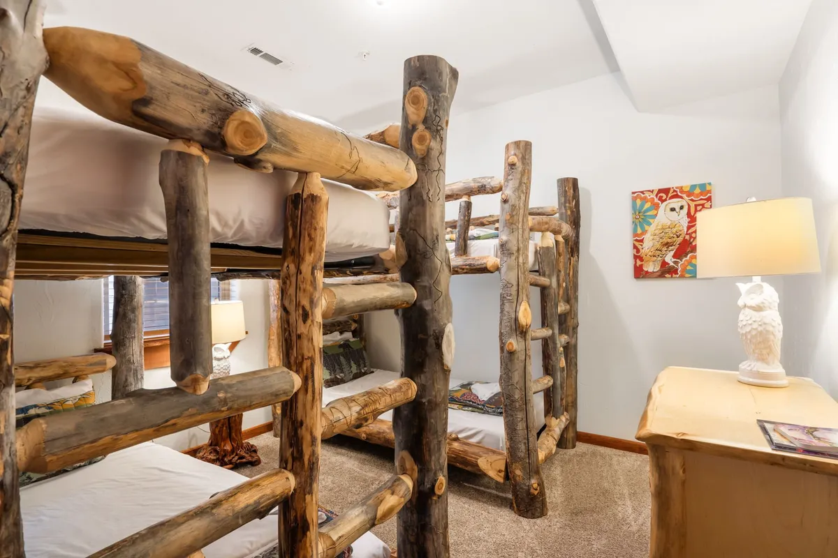 A playful bunk room featuring log-style bunk beds, whimsical owl artwork, and a glowing table lamp. The space feels inviting and imaginative, ideal for children seeking adventure and fun sleepovers.