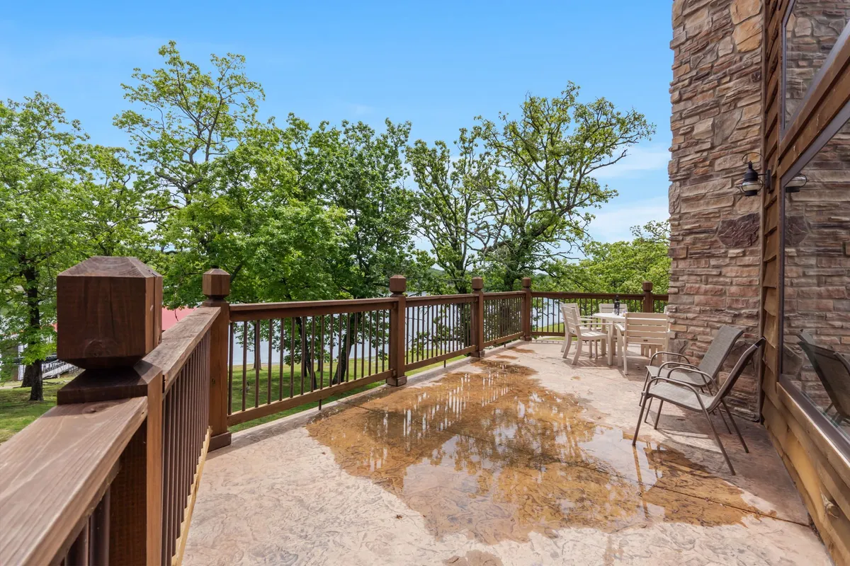 This image features a tranquil patio setting with comfortable furniture and a wooden railing, surrounded by trees and overlooking the water. The peaceful atmosphere is perfect for both relaxing and social gatherings, with hints of the lake just beyond the patio area.