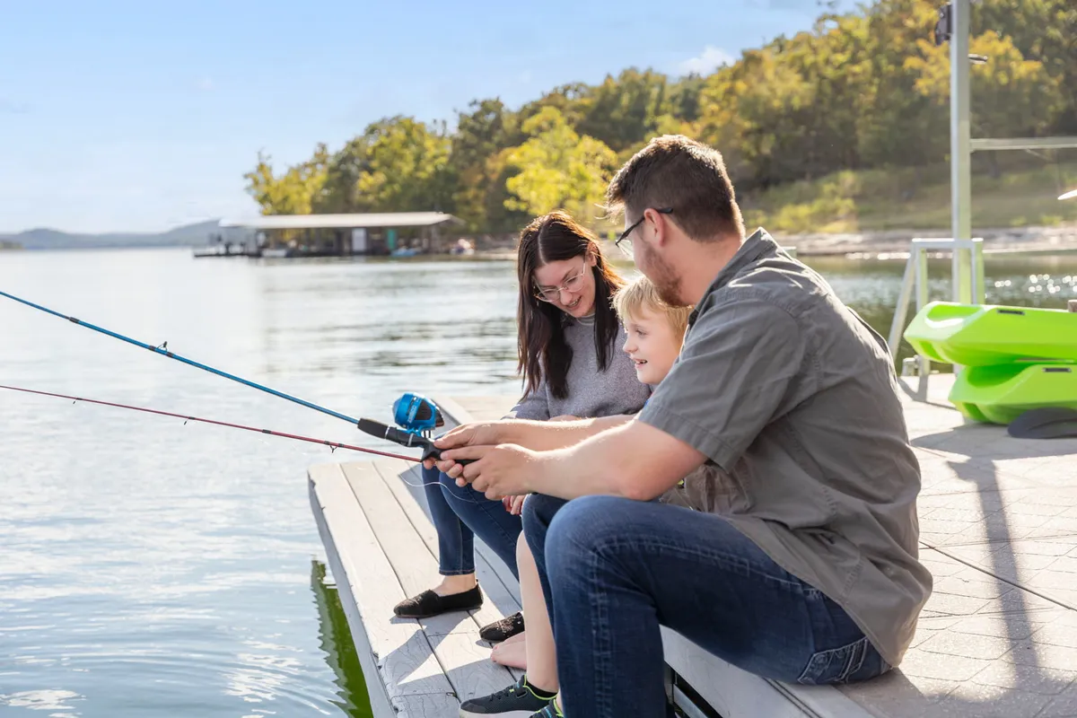A joyful moment featuring a family fishing together by the serene lake. Children and adults are engaged in fishing with rods, with the tranquil lake and natural surroundings setting a peaceful yet playful mood.