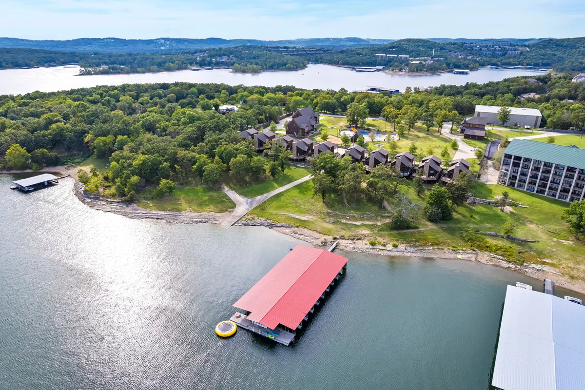 A scenic view of Table Rock Lake with a dock and multiple cabins nestled in lush greenery, inviting guests to boat, fish, or simply soak up the natural beauty. The image captures the lakeside setting and recreational opportunities available right outside the home.