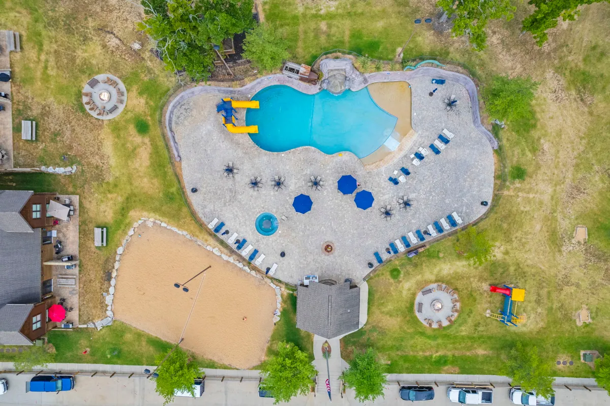 An inviting outdoor area showcasing a sparkling swimming pool with water slides, a sand volleyball court, comfortable seating areas, and a cozy fire pit. The vibrant scene is filled with opportunities for play, relaxation, and socializing among groups.