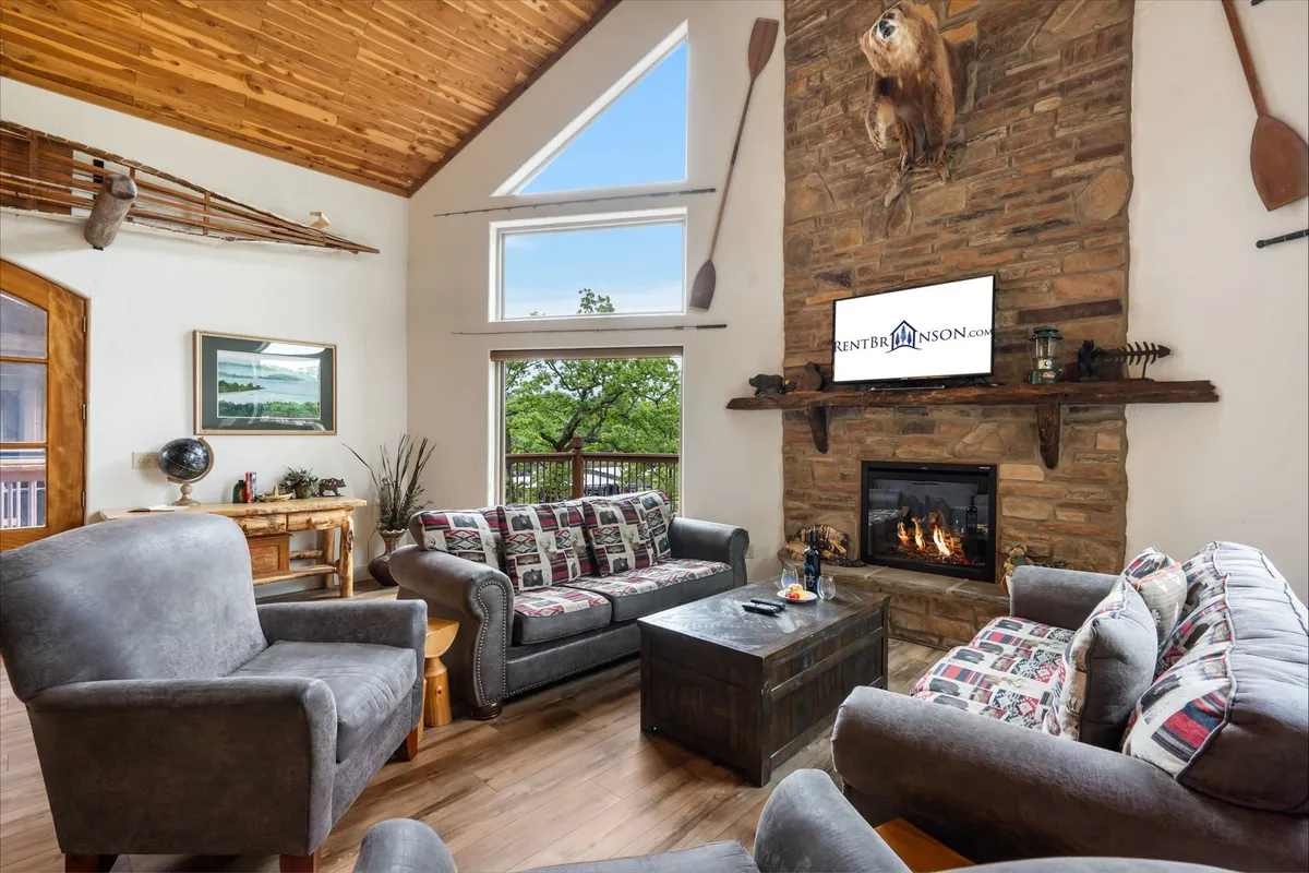 An inviting interior space with a cozy fireplace, large windows looking out to nature, a comfortable sofa arrangement, and a TV mounted on the wall. The setting feels perfect for relaxing, watching movies, or sharing stories after a day of outdoor fun.