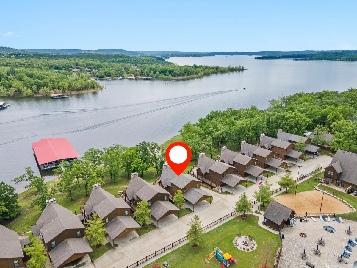A vibrant exterior scene showing Table Rock Lake in the background, cozy lakefront cabins, a family-friendly playground, and boats docked nearby. The lush green lawns and open spaces convey a welcoming atmosphere for outdoor activities and group gatherings.