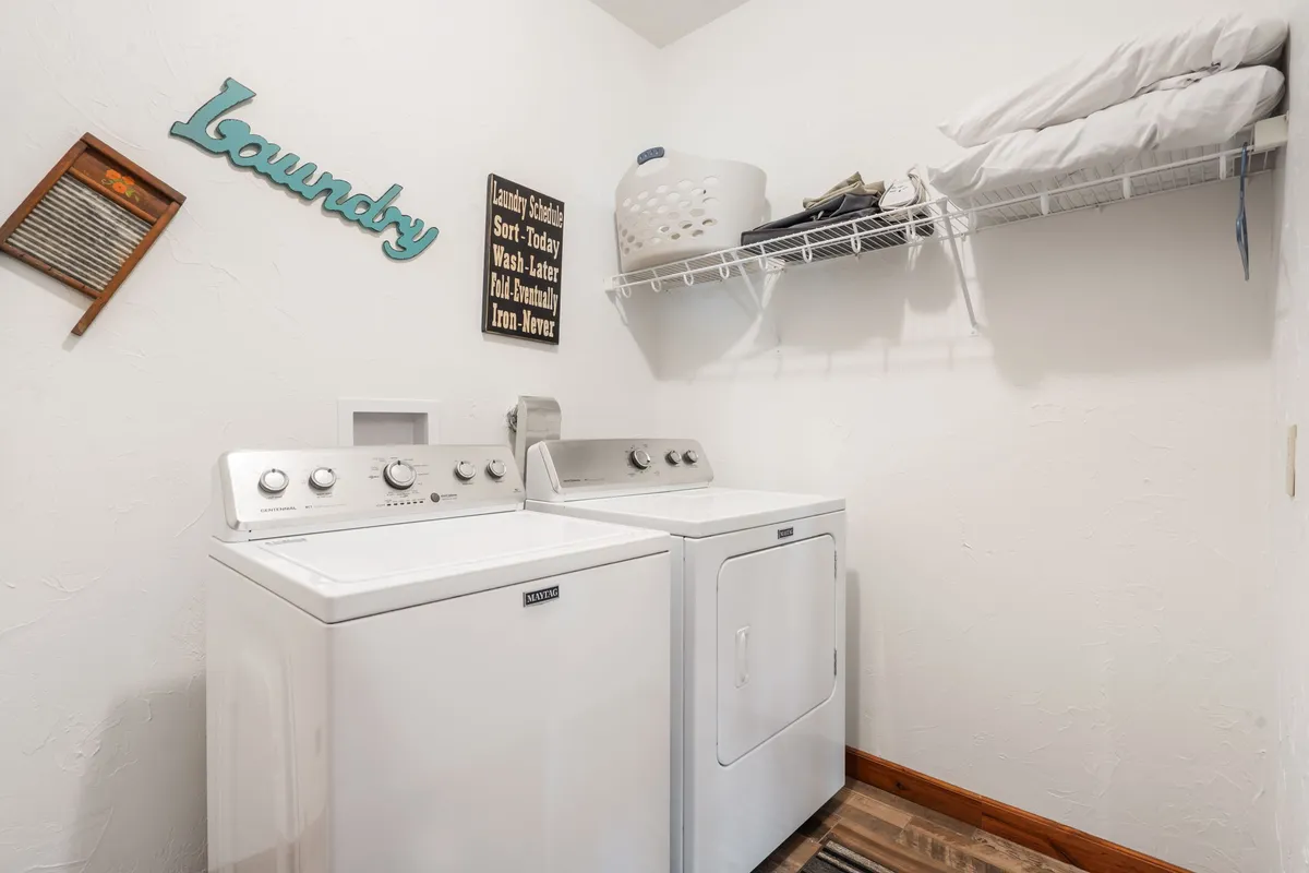 A practical laundry room featuring a washing machine, dryer, laundry sign, and neatly organized shelves with linens and a washboard, creating a fresh and functional space.