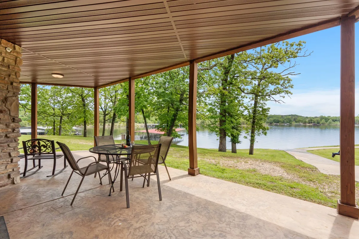 An outdoor patio table and chairs overlook a serene lake view, surrounded by lush trees. The setting invites al fresco dining, morning coffee, or simply enjoying the outdoors, seamlessly connecting the interior to nature and the lake beyond.